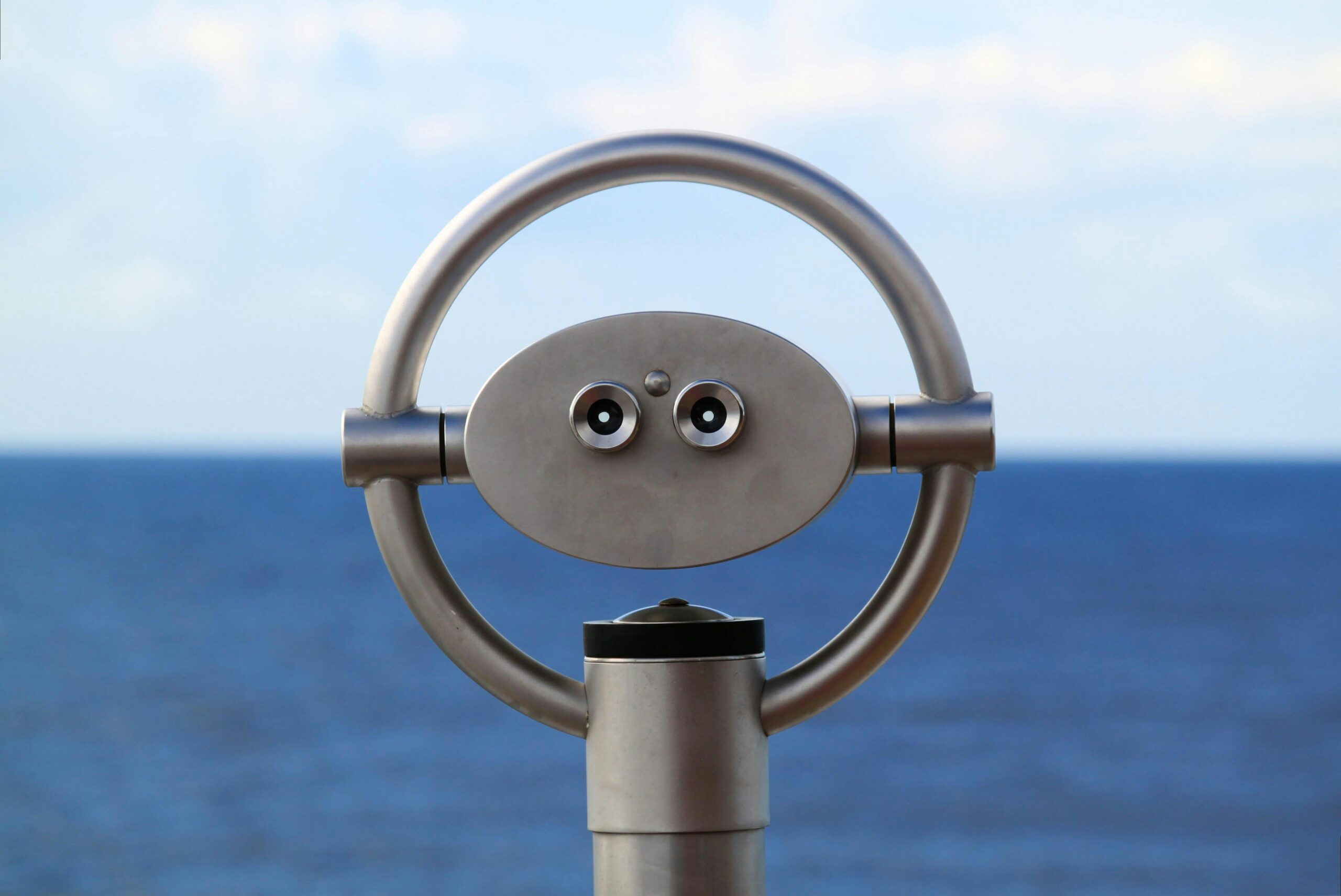 Silver public binoculars overlooking a serene ocean under a blue sky.