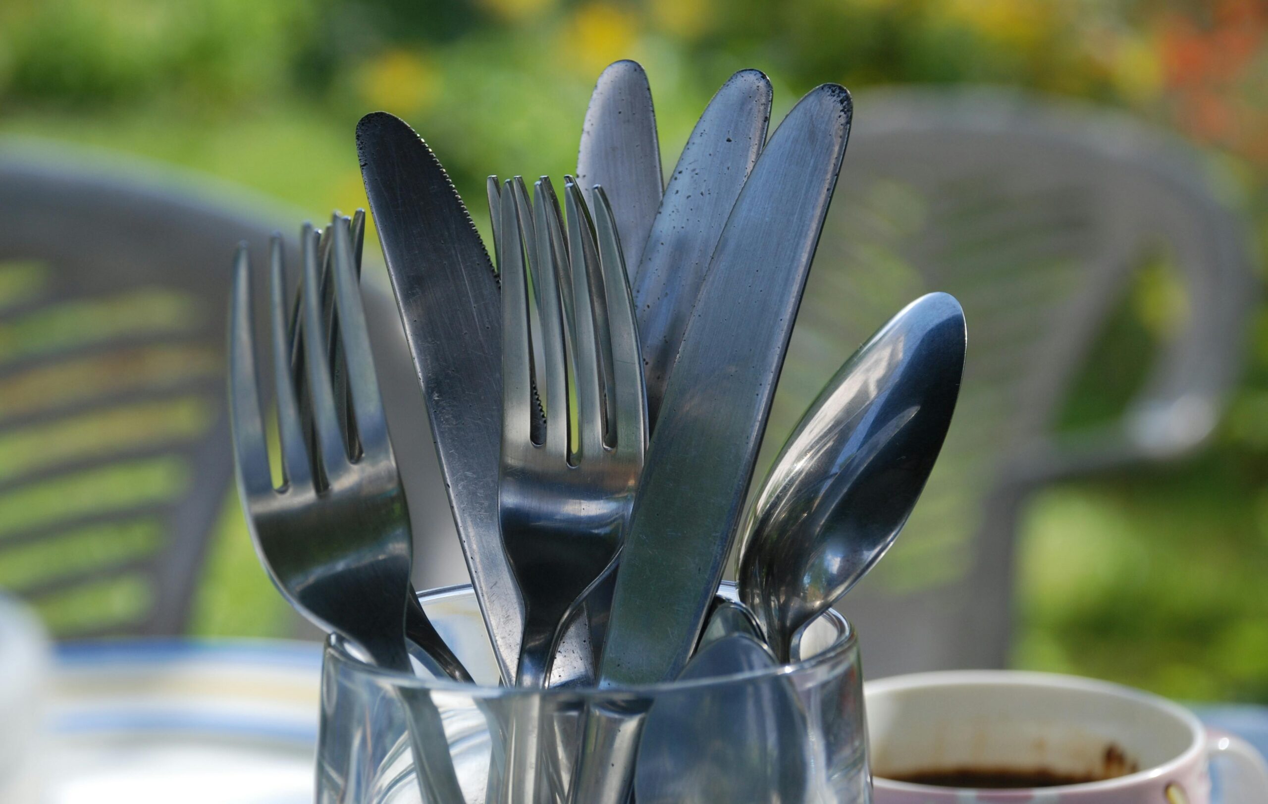 A close-up of various silverware pieces in a glass on a sunny day.